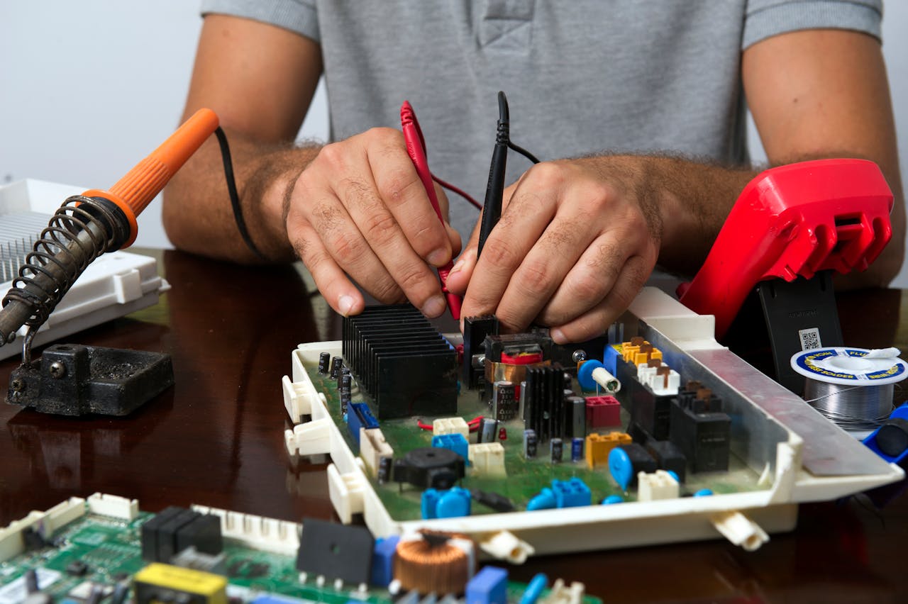 Technician skillfully repairing an electronic circuit board with various tools on a wooden table.